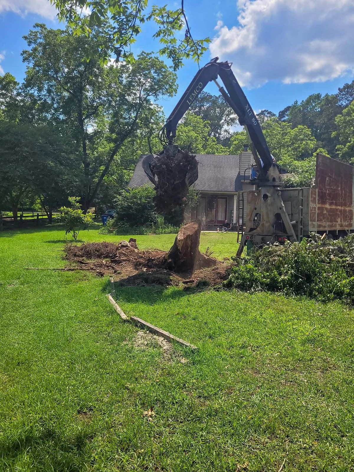 Grapple lifting a stump and root ball from a yard